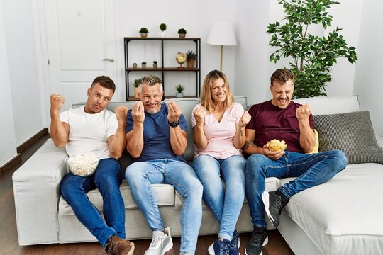 Group of middle age people sitting on the sofa at home very happy and excited doing winner gesture with arms raised, smiling and screaming for success. celebration concept.