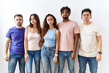 Obraz premium Group of young people standing together over isolated background puffing cheeks with funny face. mouth inflated with air, crazy expression.