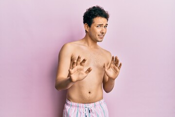 Young handsome man wearing swimwear shirtless disgusted expression, displeased and fearful doing disgust face because aversion reaction. with hands raised