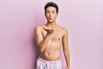 Fototapeta premium Young handsome man wearing swimwear shirtless looking at the camera blowing a kiss with hand on air being lovely and sexy. love expression.