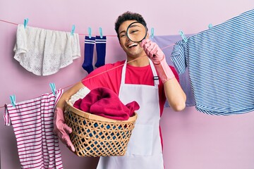Handsome hispanic man doing laundry holding wicker basket looking for a stain smiling and laughing...