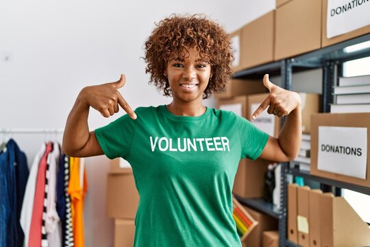 Young african american woman pointing with fingers to volunteer uniform at charity center