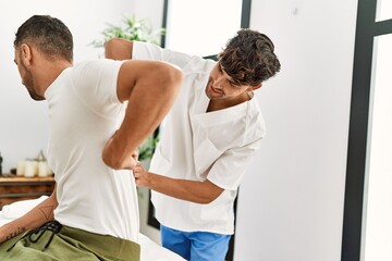Fototapeta premium Two hispanic men physiotherapist and patient having rehab session massaging back at clinic