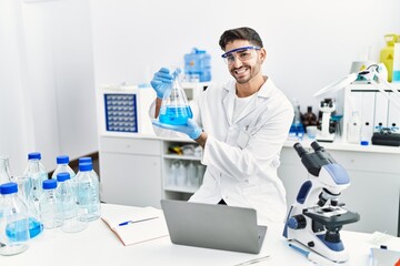 Handsome hispanic man working as scientific holding erlenmeyer flask at laboratory