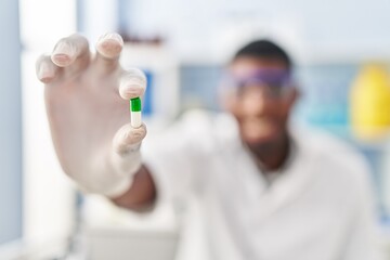 Young african american man wearing scientist uniform holding pill at laboratory