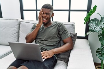 Young african american man using laptop at home sitting on the sofa yawning tired covering half face, eye and mouth with hand. face hurts in pain.