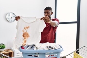 Young african american man holding dirty clothes at laundry room