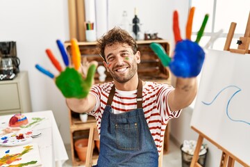 Young hispanic man smiling confident showing colored palm hands at art studio