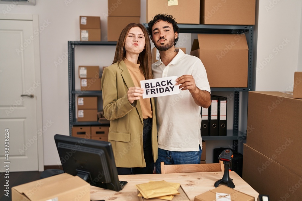 Wall mural Young two people holding black friday banner at small business store puffing cheeks with funny face. mouth inflated with air, catching air.