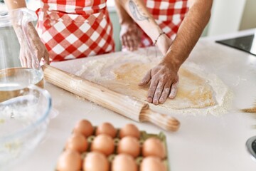 Young couple smiling happy kneading dough with hands at kitchen.