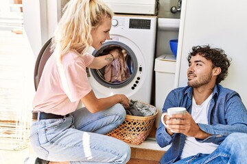 Young couple smiling happy drinking coffee while doing laundry at home.