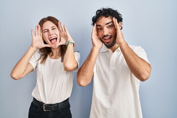 Young couple wearing casual clothes standing together smiling cheerful playing peek a boo with hands showing face. surprised and exited