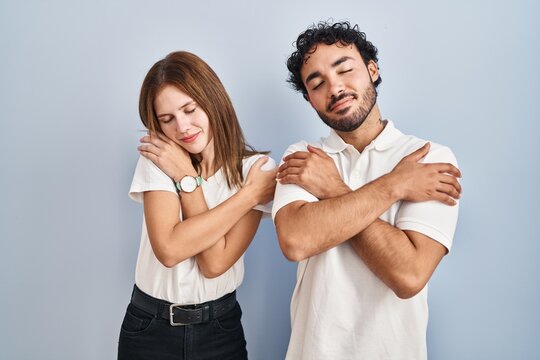 Young couple wearing casual clothes standing together hugging oneself happy and positive, smiling confident. self love and self care