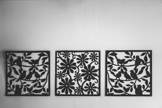 Black metal cut decoration frame hanging on the white wall. Ornamental laser cut birds and flowers