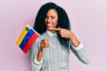 Middle age african american woman holding venezuelan flag smiling happy pointing with hand and finger