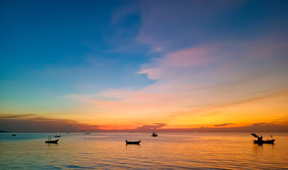 Fototapeta premium Sky and sea at sunset, local boats floating in the middle of the sea, orange and blue sky reflecting the sea, giving a calm feeling.