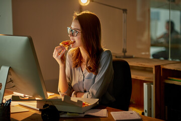 Late night meals in the office. Shot of an attractive young businesswoman eating pizza while working late in the office.