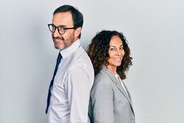 Middle age couple of hispanic woman and man wearing business office uniform looking to side, relax profile pose with natural face with confident smile.