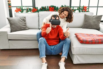 Obraz premium Middle age hispanic couple smiling happy sitting on the sofa playing with virtual reality glasses at home.