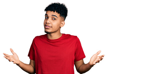 Young african american man wearing casual red t shirt clueless and confused expression with arms...