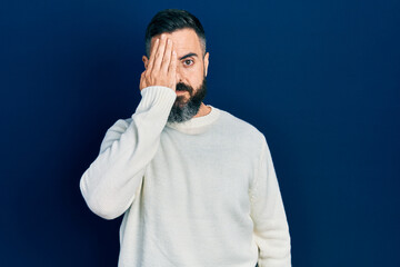 Young hispanic man wearing casual clothes covering one eye with hand, confident smile on face and surprise emotion.
