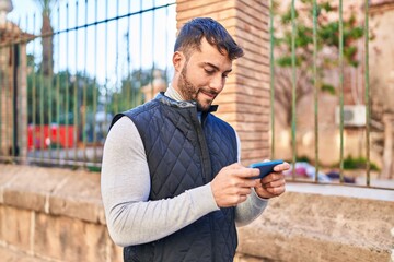 Fototapeta premium Young hispanic man smiling confident using smartphone at street