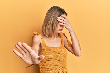 Young caucasian blonde woman wearing casual yellow t shirt covering eyes with hands and doing stop...