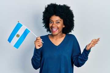 Young african american woman holding argentina flag celebrating achievement with happy smile and...