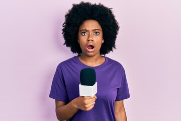 Young african american woman holding reporter microphone afraid and shocked with surprise and...