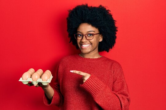 Young african american woman showing fresh white eggs smiling happy pointing with hand and finger