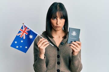 Young hispanic woman holding australian flag and passport skeptic and nervous, frowning upset...