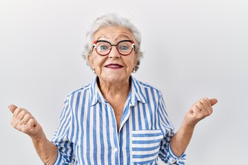 Senior woman with grey hair standing over white background celebrating surprised and amazed for success with arms raised and open eyes. winner concept.