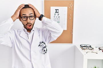 African american optician man standing by eyesight test crazy and scared with hands on head, afraid and surprised of shock with open mouth