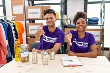 Young interracial people wearing volunteer t shirt at donations stand smiling friendly offering handshake as greeting and welcoming. successful business.