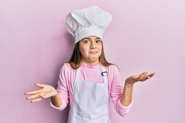 Beautiful brunette little girl wearing professional cook apron and hat clueless and confused with...