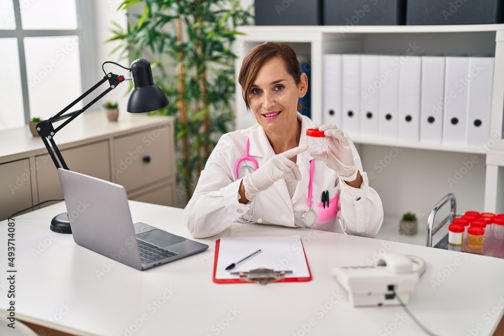 Wall mural Middle age woman wearing doctor uniform holding empty analysis test tube at clinic