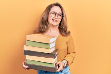 Middle age caucasian woman holding a pile of books winking looking at the camera with sexy expression, cheerful and happy face.