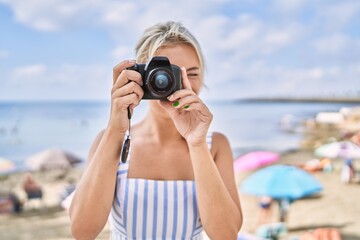 Young blonde girl smiling happy using camera at the beach.