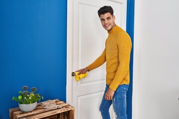 Young hispanic man smiling confident cleaning door knob at home