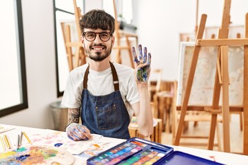 Hispanic man with beard at art studio showing and pointing up with fingers number four while smiling confident and happy.