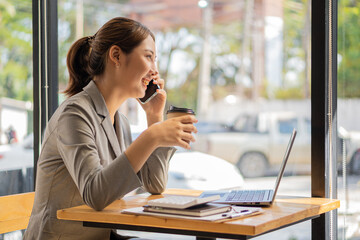 Young Asian woman using phone and laptop in coffee shop attractive young woman businesswoman smiling and talking on mobile phone in the office