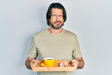 Middle age caucasian man holding breakfast tray with cookies and coffee skeptic and nervous, frowning upset because of problem. negative person.