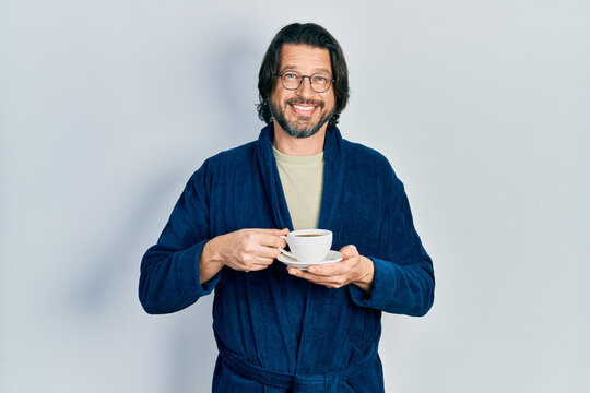 Middle age caucasian man wearing robe drinking coffee smiling with a happy and cool smile on face. showing teeth.