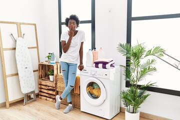 African young woman doing laundry at home covering mouth with hand, shocked and afraid for mistake....