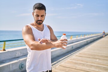 Hispanic sports man wearing workout style applying sunscreen on arm outdoors on a sunny day
