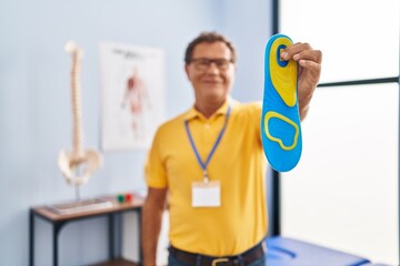 Middle age man podiatrist holding insole at physiotherpy clinic