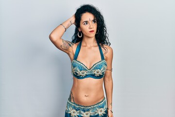 Fototapeta premium Young woman wearing bindi and traditional belly dance clothes confuse and wondering about question. uncertain with doubt, thinking with hand on head. pensive concept.