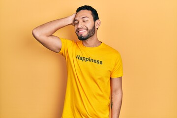 Hispanic man with beard wearing t shirt with happiness word message smiling confident touching hair with hand up gesture, posing attractive and fashionable