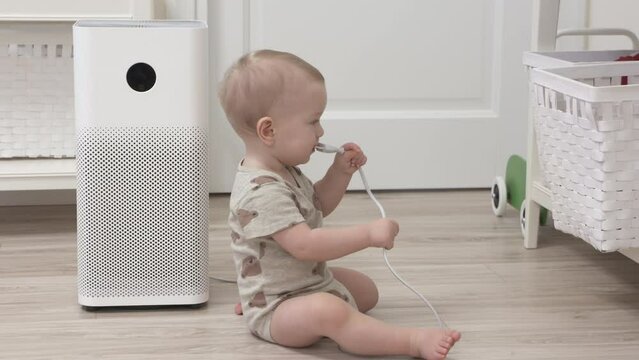 Risky objects around the house for 1 year old baby boy, kid playing with electric wire attached to appliance, infant holding the electric cord of air purifier in the room. High quality 4k footage
