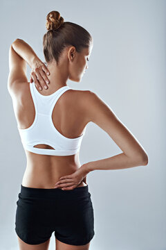 Stretching her back out. Studio shot of an athletic young woman holding her neck and back in pain against a grey background.